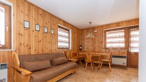 A wooden-paneled room with a sofa, dining table, chairs, and a radiator. - Casa Coli (Mazzin)