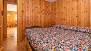 A wooden-paneled room with a bed, a heater, and a door leading to a dining area. - Casa Coli (Mazzin)