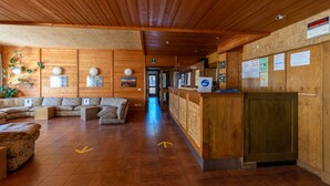 A wooden interior with a reception desk, sofas, and directional arrows on the floor. - Petit Arnica (Selva di Cadore)