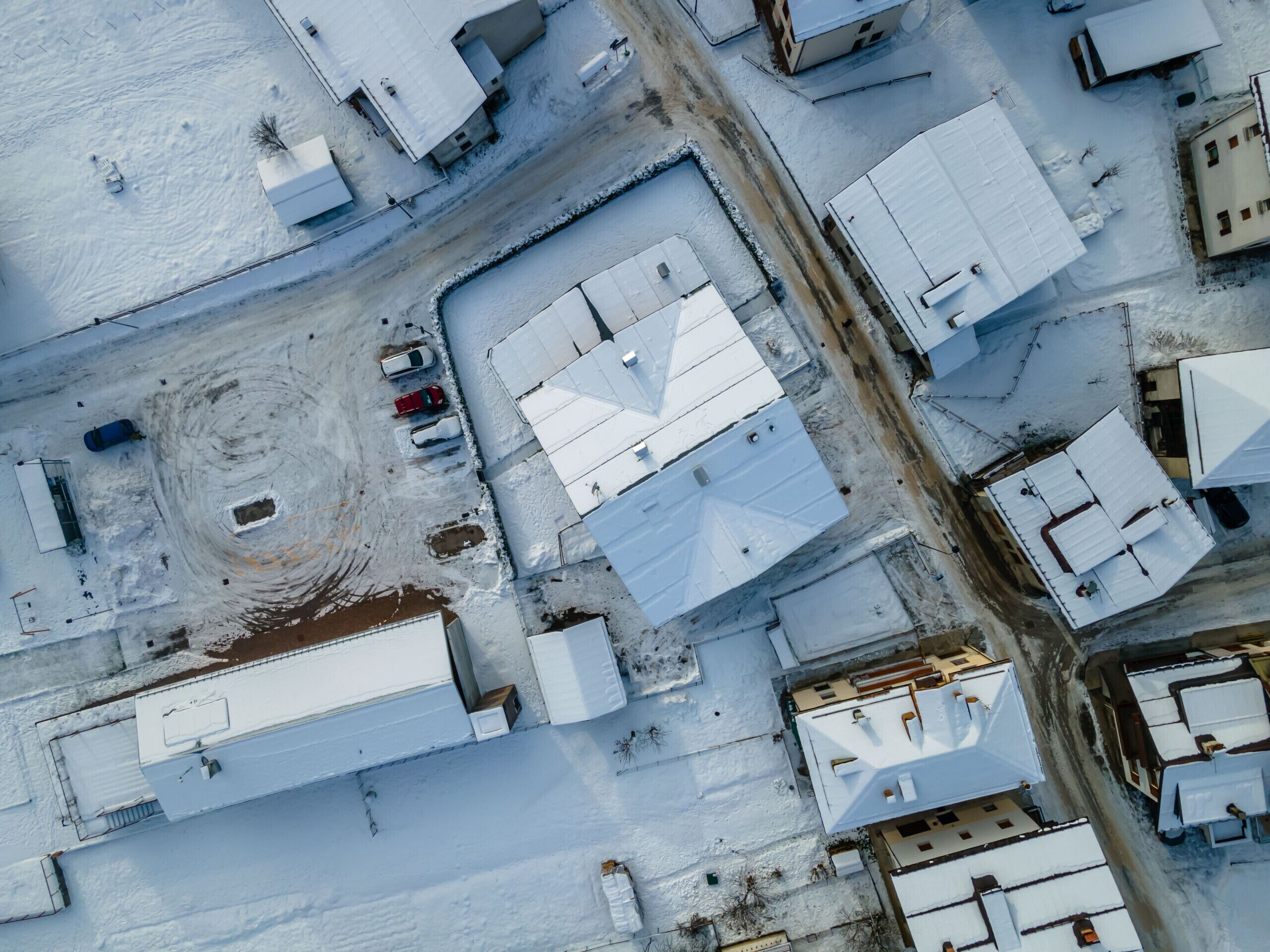 Vista aerea di una zona industriale innevata con edifici grandi, una strada sterrata e veicoli parcheggiati.