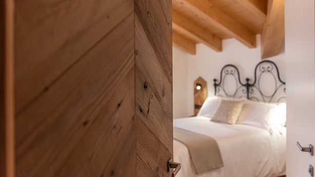 Een houten deur die leidt naar een slaapkamer met een bed, hoofdeinde en nachtkastje.