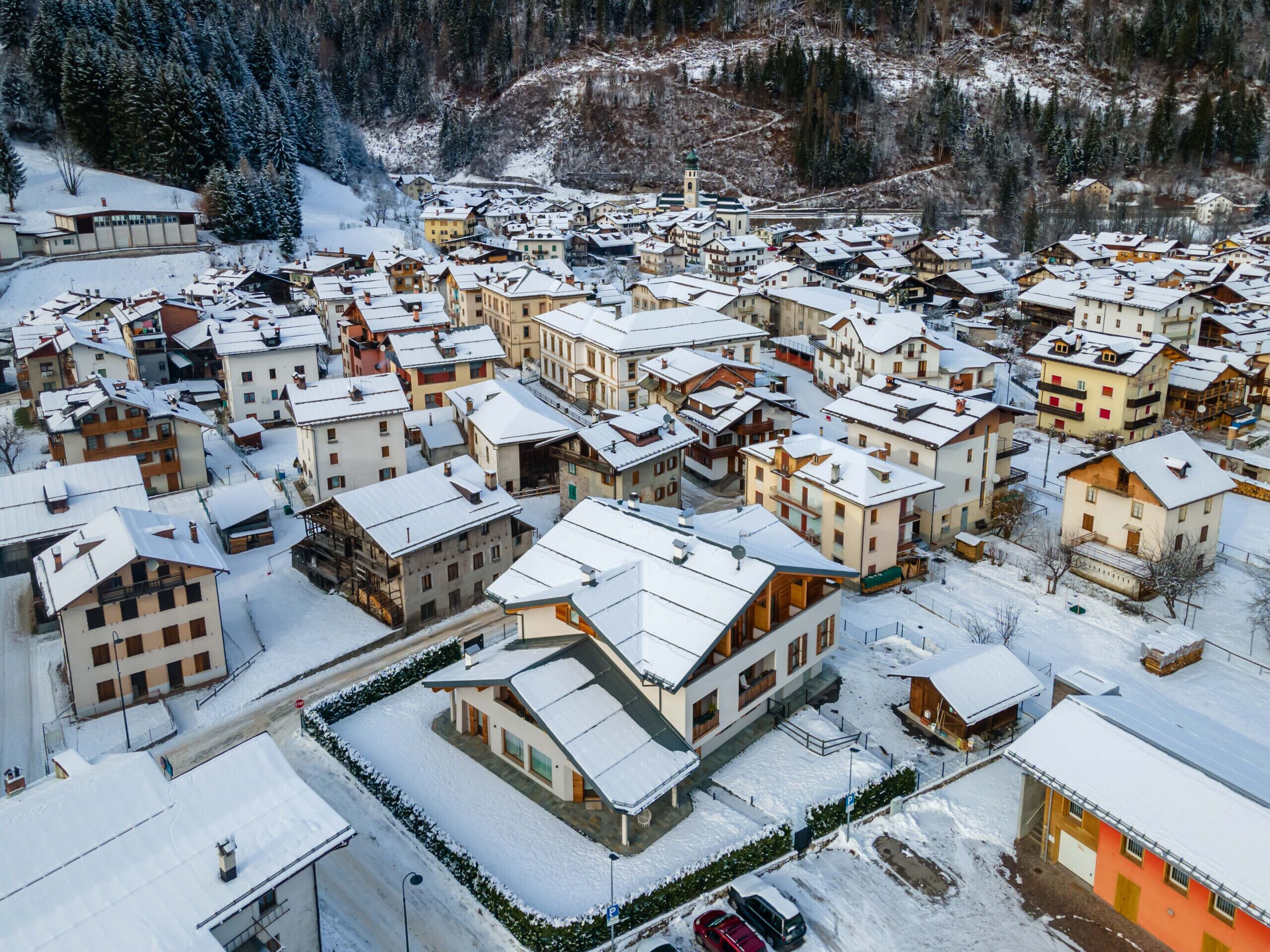A snow-covered village with traditional buildings, a central church, and a mountain backdrop.