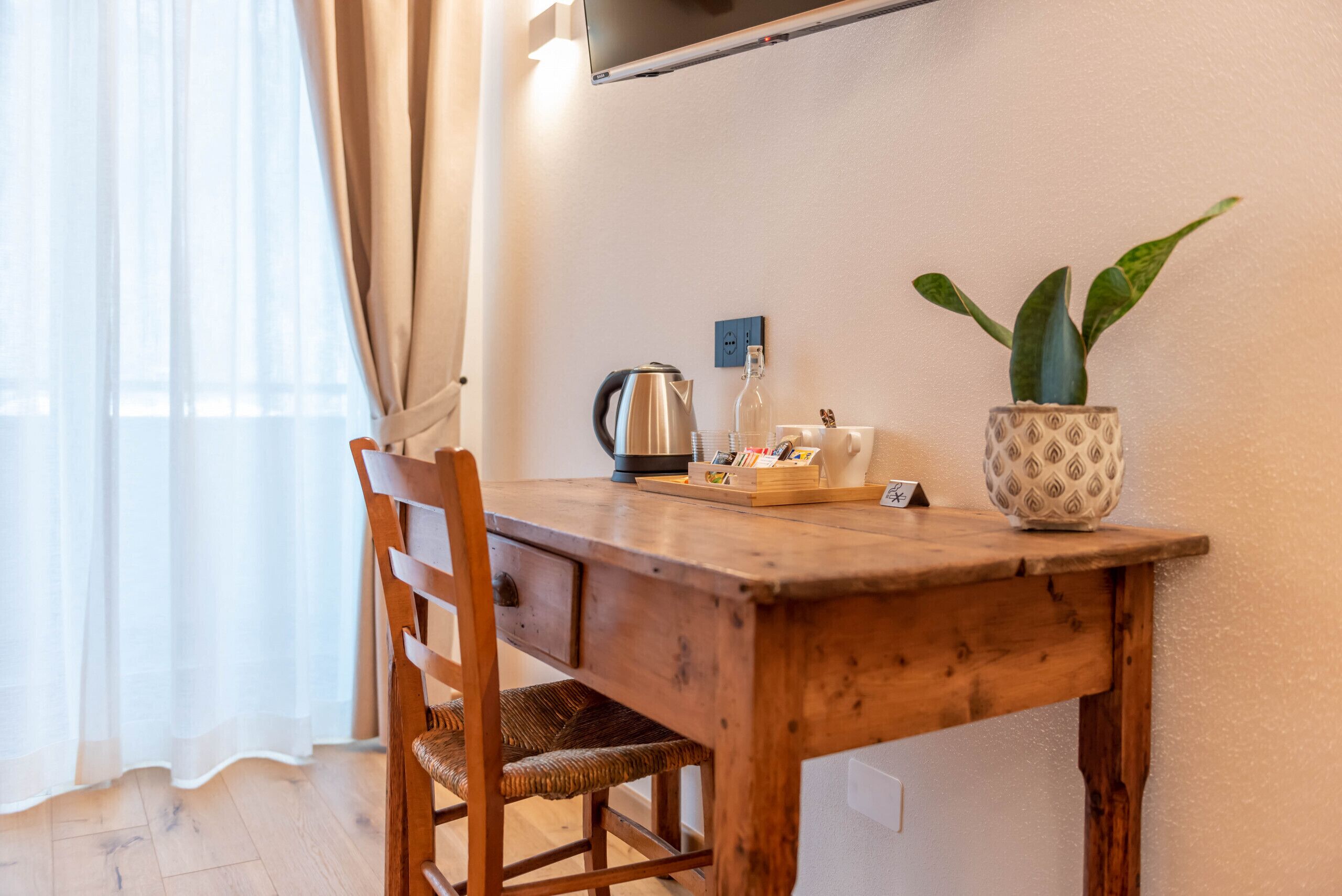Une table à manger en bois, avec une chaise, une plante en pot, une bouilloire et un verre d’eau posés sur la table.