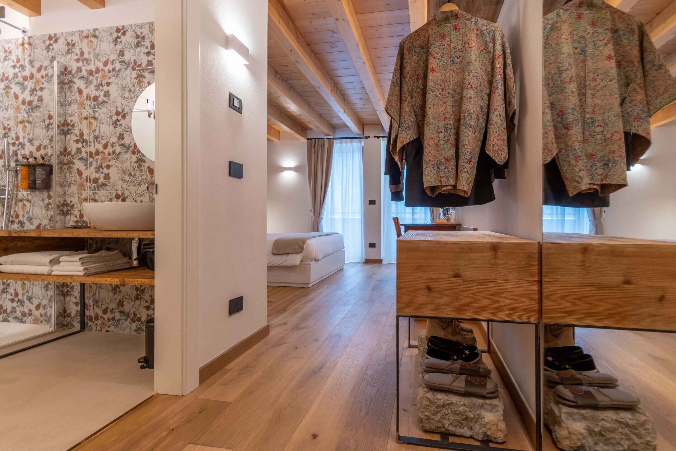 Un intérieur moderne avec un plancher en bois, un canapé blanc, une coiffeuse en bois où sont rangées des chaussures et un mur orné d’un motif floral.
