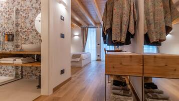 Un intérieur moderne avec un plancher en bois, un canapé blanc, une coiffeuse en bois où sont rangées des chaussures et un mur orné d’un motif floral.