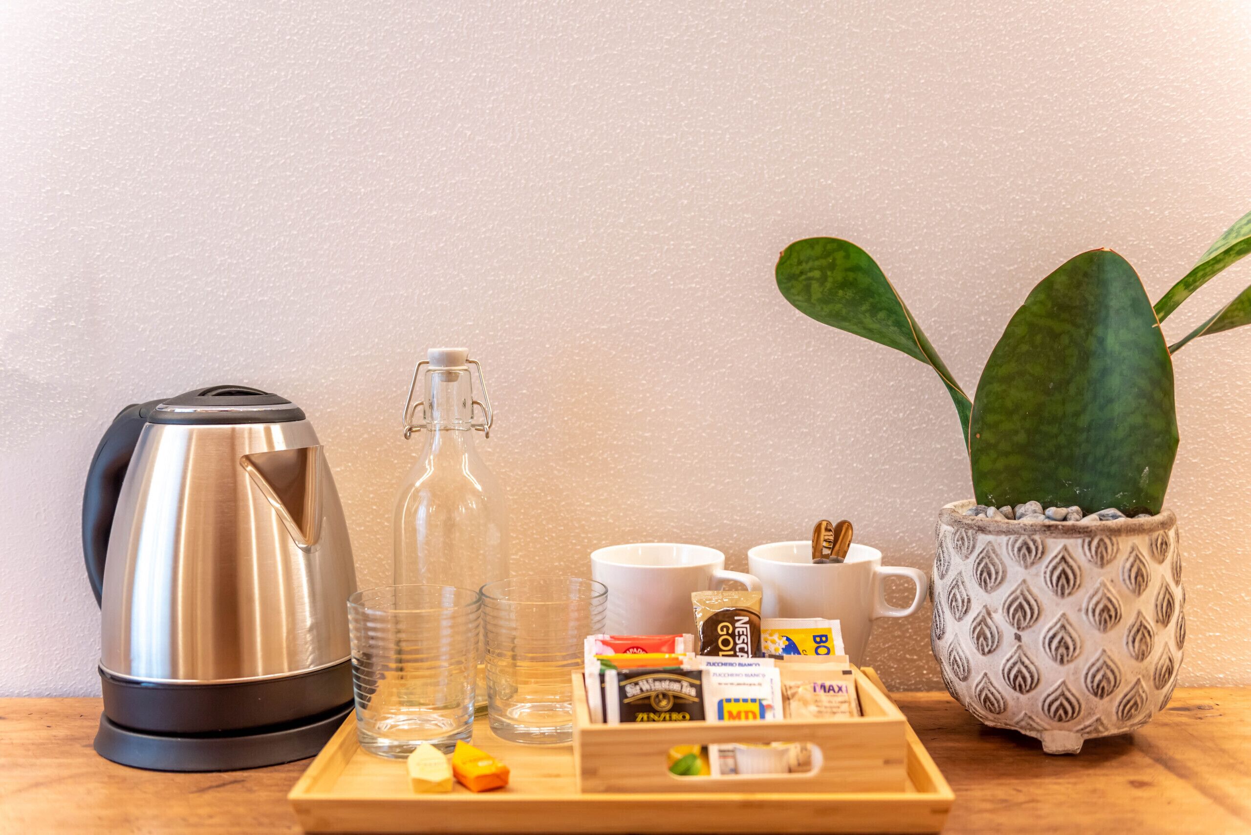 A breakfast setup with a kettle, glass pitcher, cups, and a tray with food items.