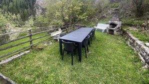 A rustic outdoor dining area with a long table and chairs, surrounded by a wooden fence and lush greenery. - Casa Narciso (Rocca Pietore)