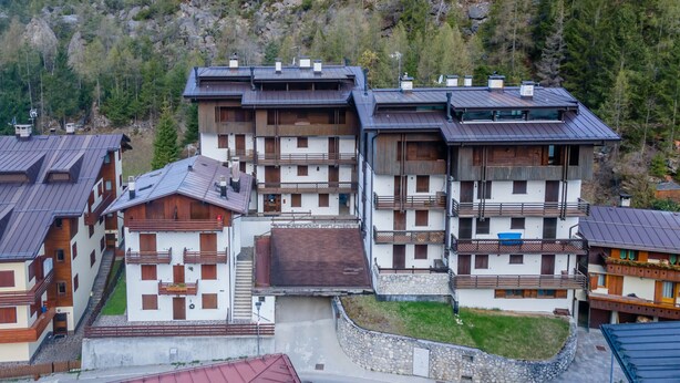 Un immeuble à plusieurs étages doté de balcons, d’un mur de soutènement en pierre et surplombant un paysage montagneux.