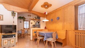A cozy kitchen with wooden cabinets, a dining table with chairs, a television, and a ceiling fan. - Casa Soreje (Mazzin)