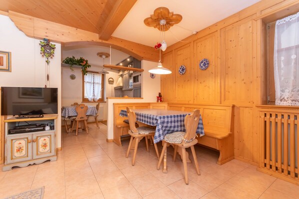 A cozy kitchen with wooden cabinets, a dining table with chairs, a television, and a ceiling fan.
