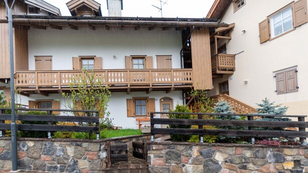 A multi-story building with wooden balconies and a stone wall in front. - Casa Soreje (Mazzin)