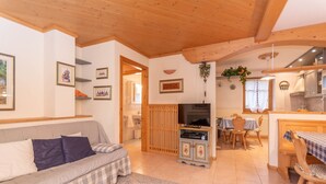 A cozy living room with a sofa, a television, a dining area with a table and chairs, and a kitchen area. - Casa Soreje (Mazzin)