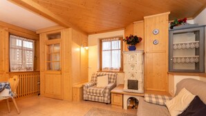 A cozy wooden interior with a checkered armchair, a sofa, a cabinet with decorative plates, and a small table with a vase of flowers. - Casa Soreje (Mazzin)
