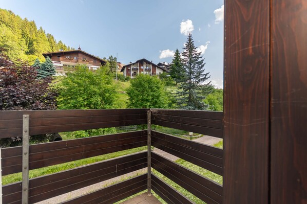 A wooden balcony with a view of a mountain house and surrounding greenery.