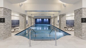A large indoor swimming pool with stone walls and a blue-tiled floor.