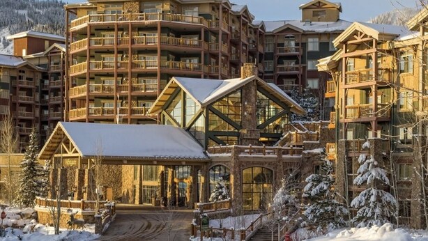 A multi-story lodge with a central glass atrium, wooden balconies, and a snow-covered landscape.