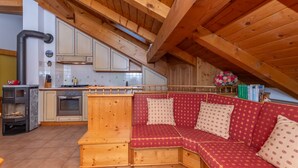A cozy kitchen with wooden beams, a built-in stove, and a red upholstered bench. - mansarda Lungolago (Alleghe)