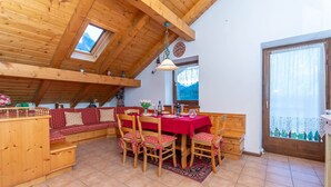 A cozy dining area with wooden furniture, a red tablecloth, and a view of the mountains through a window. - mansarda Lungolago (Alleghe)