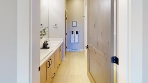 Un pasillo estrecho con un lavabo blanco, armarios de madera y una puerta con perchero.