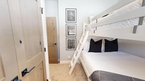 A bunk bed room with a ladder, a door, and three framed pictures on the wall.