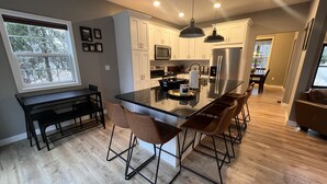 Una cocina moderna con una isla central, armarios blancos, electrodomésticos de acero inoxidable y una zona de comedor con taburetes de bar.