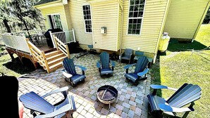 Un patio con sillas Adirondack, un hogar para fuego y una terraza de madera que conduce a una casa.