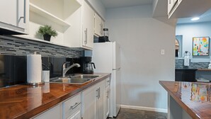 Eine moderne Küche mit weißen Schränken, einer Holz Arbeitsplatte, einer Spüle, einem Kühlschrank und einer Kaffeemaschine.