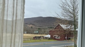 A rural landscape with a red barn, a road, and a hill in the background.