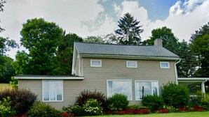A two-story house with a front porch, a lawn, and a garden with red flowers.