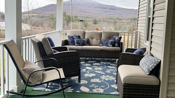 A covered porch with a seating area featuring wicker furniture and a decorative rug.