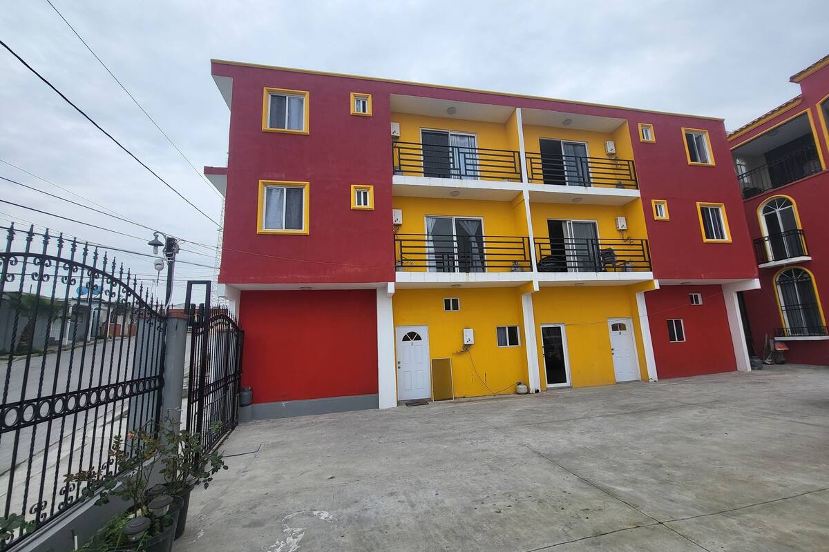 A multi-story building with a red and yellow facade, balconies, and a gated entrance.