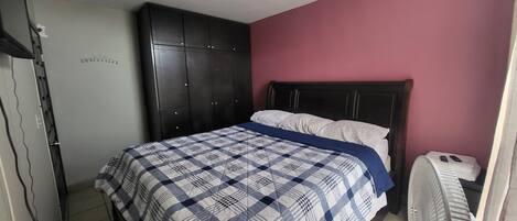 A bedroom with a bed, a wardrobe, a ceiling fan, and a door.