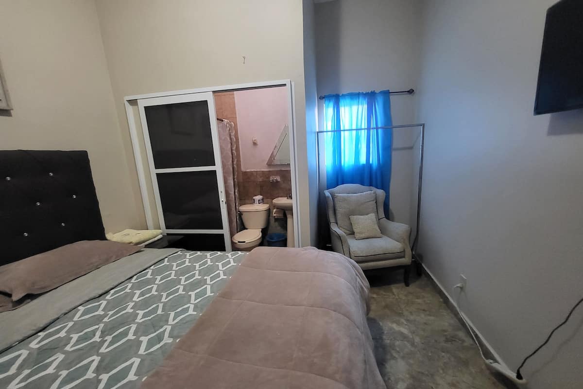 A bedroom with a bed, a chair, a toilet, and a shower area.