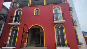 A multi-story building with a red facade, yellow trim, and black metal railings. - Departamentos velasco (Tijuana)