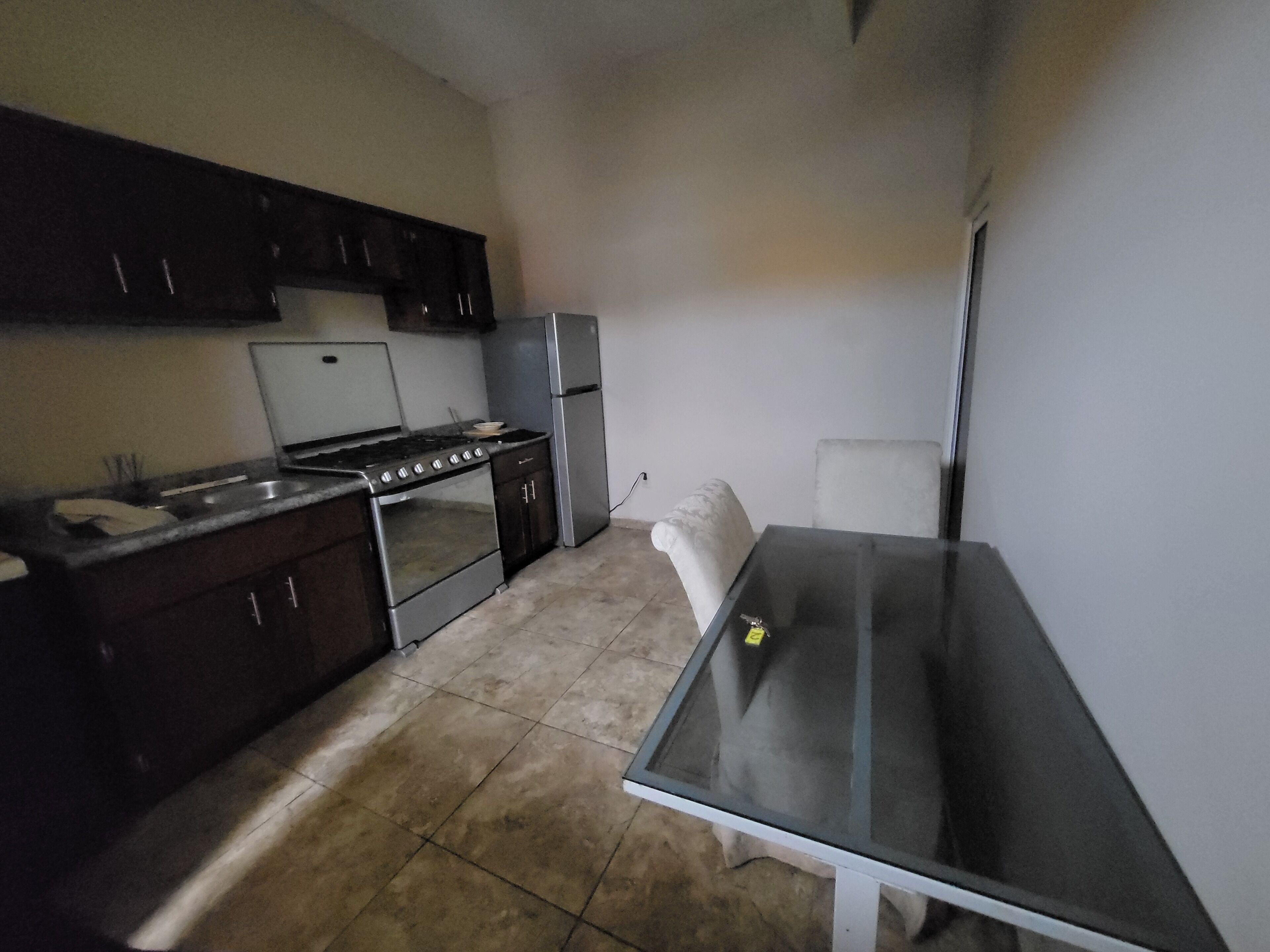 Una cocina compacta con armarios oscuros, una estufa, un refrigerador y una pequeña mesa de comedor.