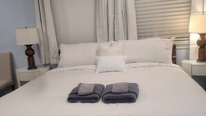 A neatly made bed with a white duvet, two folded towels, and a wooden headboard. - STUDIO COMFORT (Stanton)