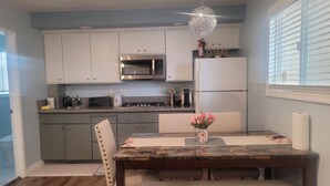 A kitchen with white cabinets, a microwave, a stove, and a refrigerator. There is a dining table with a vase of flowers and a bench. - STUDIO COMFORT (Stanton)