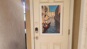 A door with a framed picture of a canal scene, a doormat, and a shoe on the floor. - STUDIO COMFORT (Stanton)