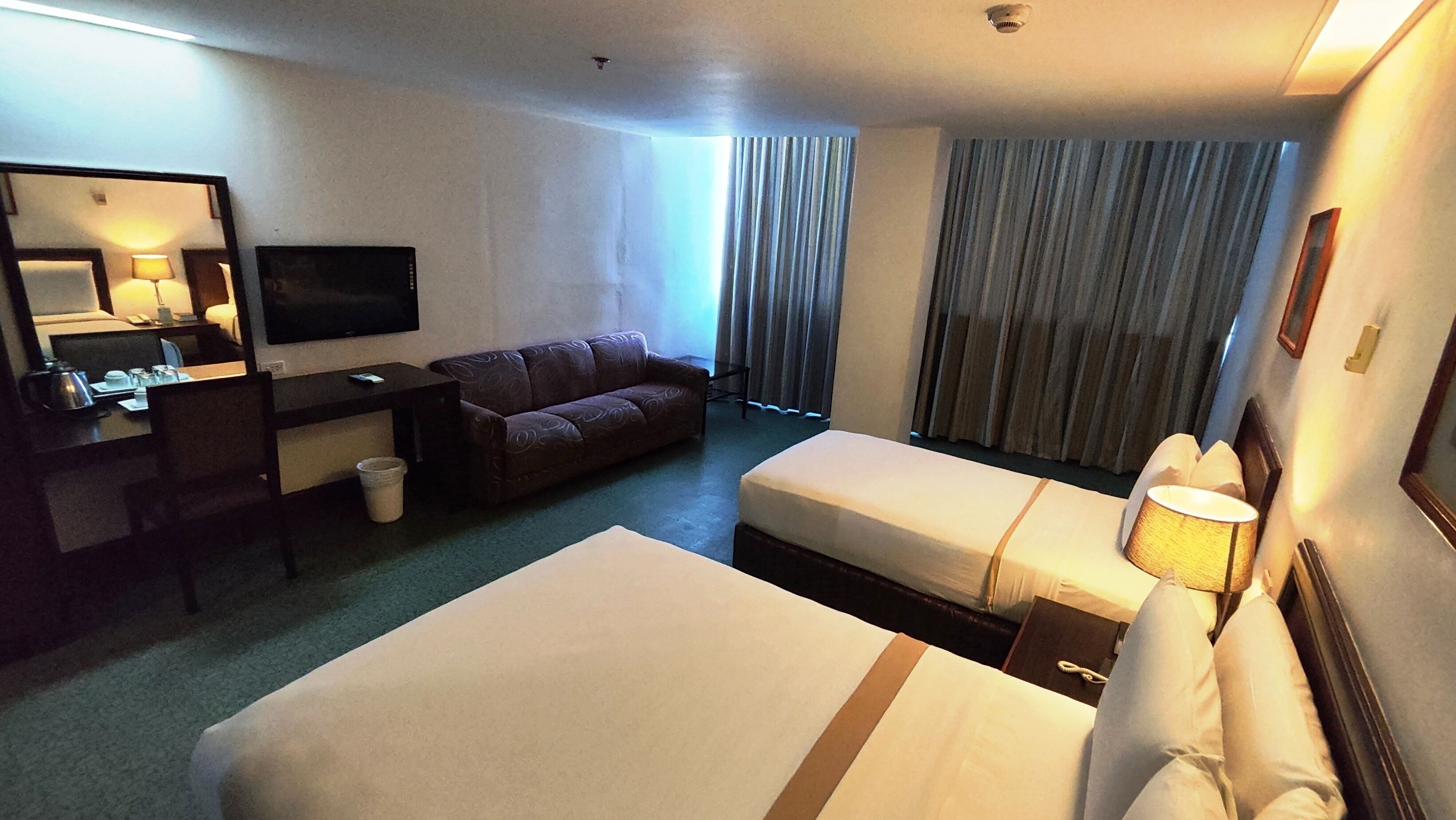 Habitación de hotel con dos camas, un escritorio, televisor, sofá y un ventanal con cortinas.