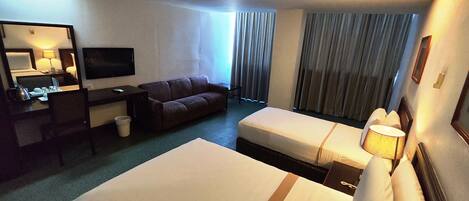 Habitación de hotel con dos camas, un escritorio, televisor, sofá y un ventanal con cortinas.