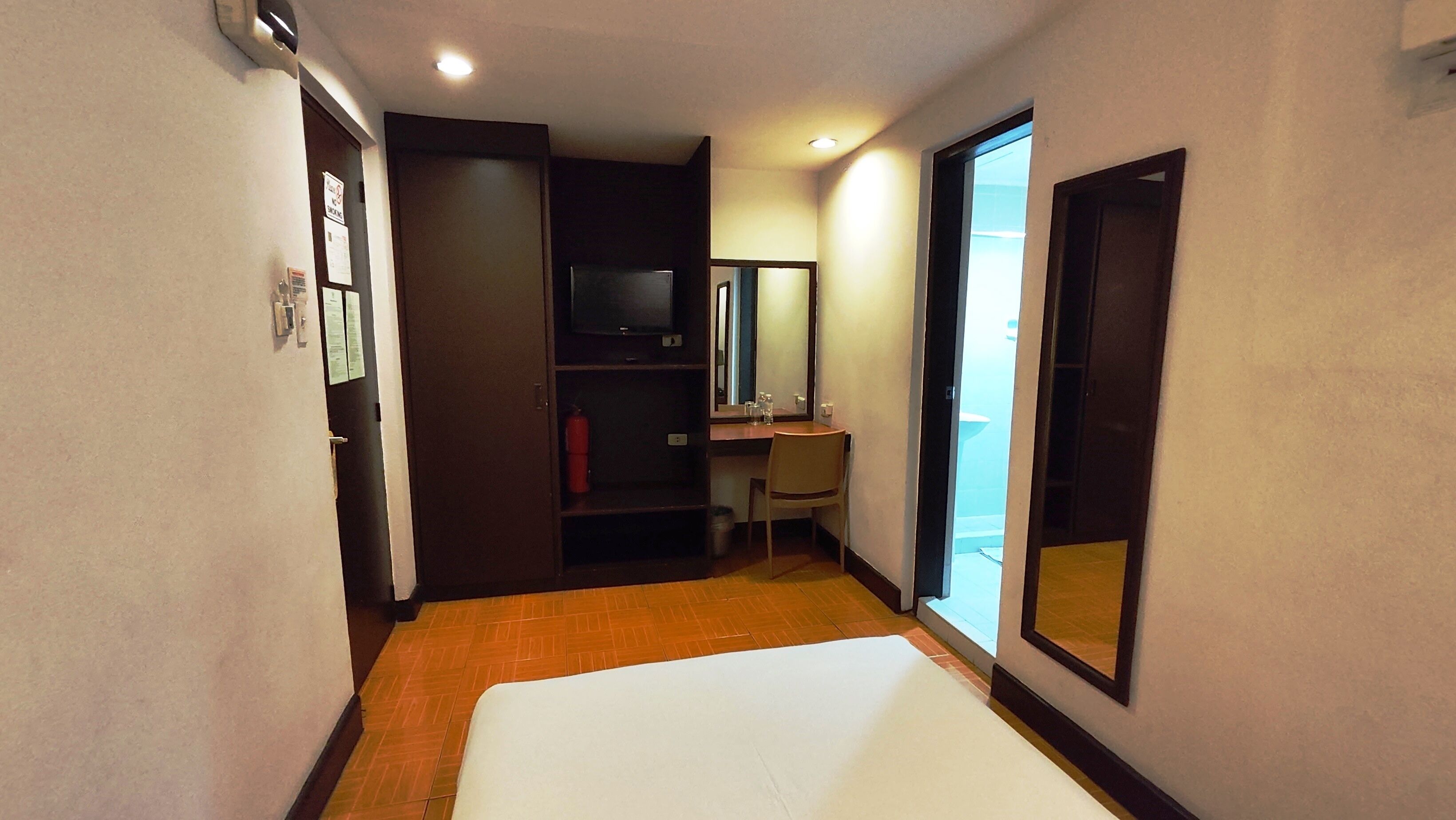 Una habitación de hotel con cama, escritorio, silla, espejo y armario.