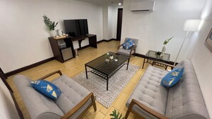 A living room with two grey sofas, a glass coffee table, a TV, and a small side table with decorative items. - Rajah Park Hotel by Hiverooms (Cebu City)