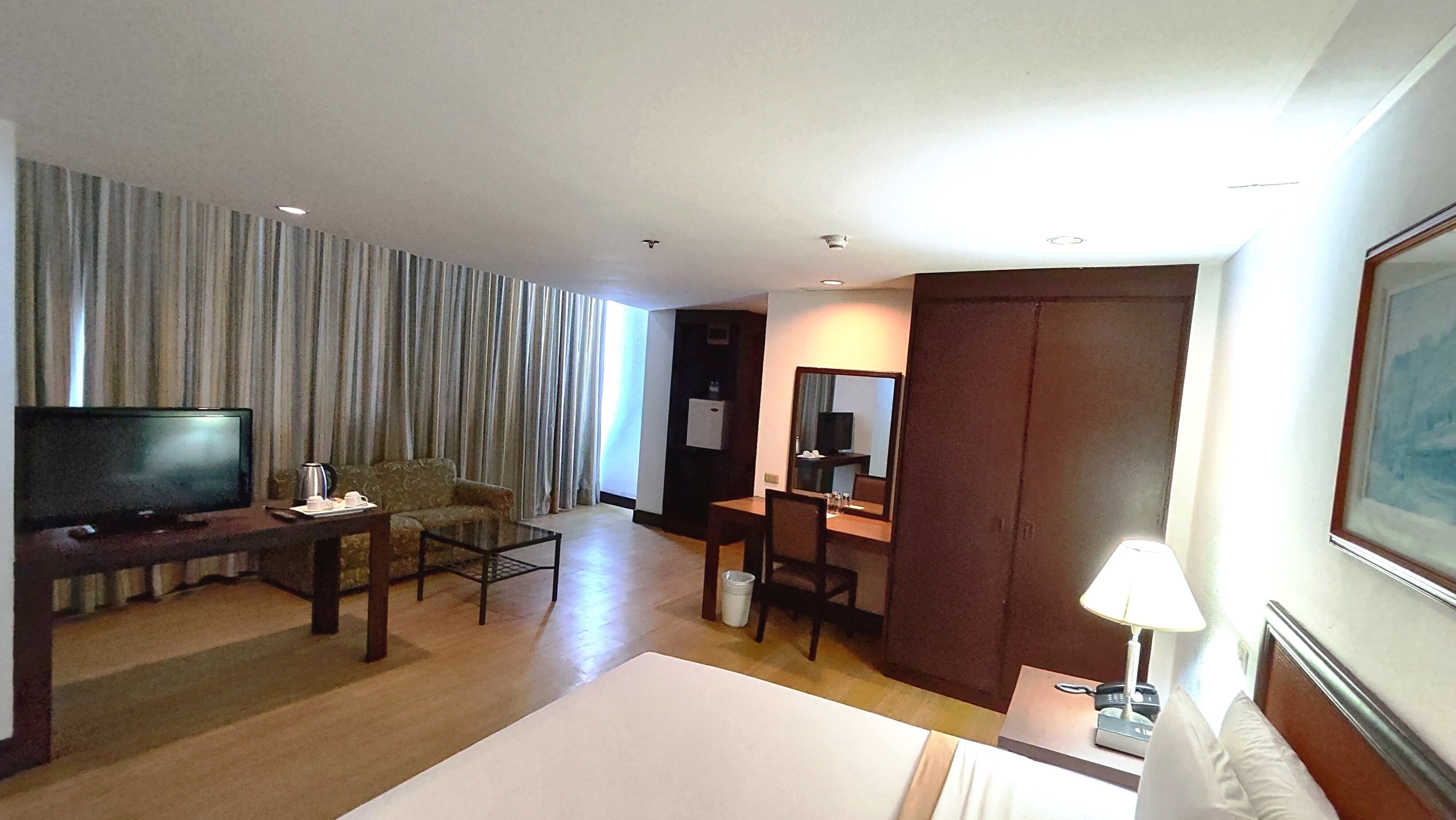 A hotel room with a flat-screen TV, a sofa, a dining table, a small table with a lamp, and a bed.