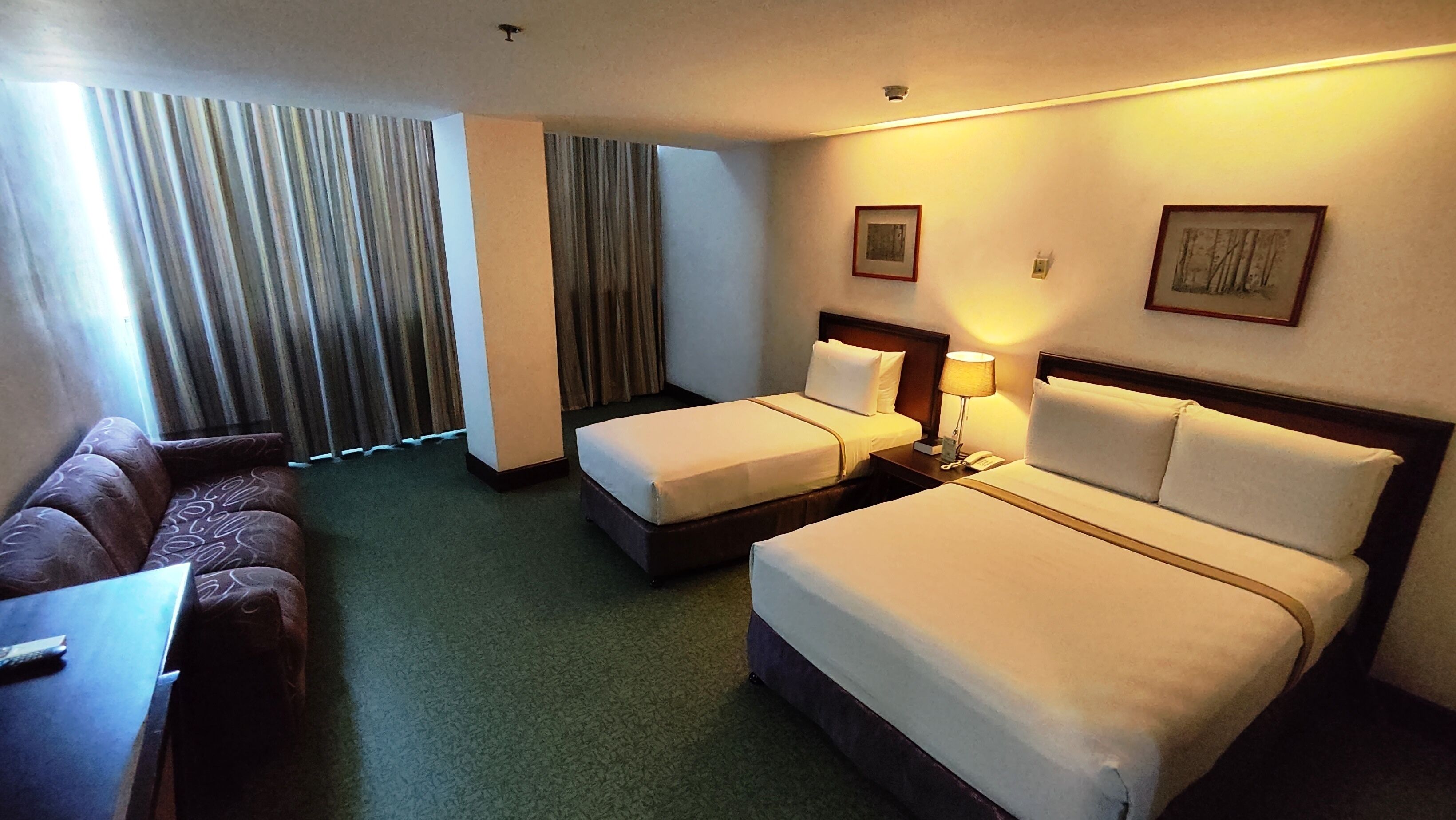 A hotel room with two single beds, a sofa, a desk, and a window with curtains.