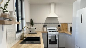 Une cuisine moderne équipée d’une cuisinière à gaz, d’un four et d’un évier. Une fenêtre offre une vue agréable, et on y trouve également une plante et un panier posés sur le plan de travail.