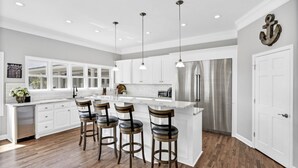 A modern kitchen with white cabinetry, a stainless steel refrigerator, and a central island with bar stools.