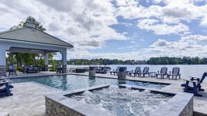 A pool area with lounge chairs and a hot tub, overlooking a lake.