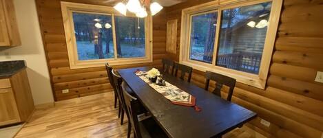 Interior de una cabaña de madera con una mesa de comedor, sillas y un ventilador de techo.