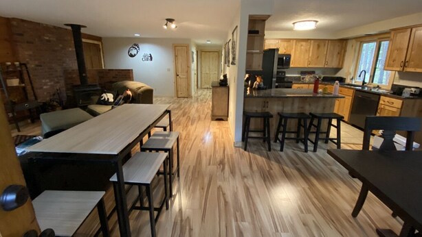 A modern kitchen with a central island, wooden flooring, and a brick accent wall. - Sweet Retreat Cozy Cabin (Sisters)