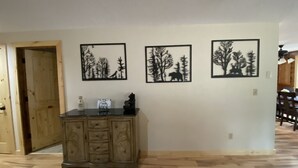 A room with a wooden floor, a cabinet with drawers, and three framed pictures on the wall depicting trees and a bear. - Sweet Retreat Cozy Cabin (Sisters)